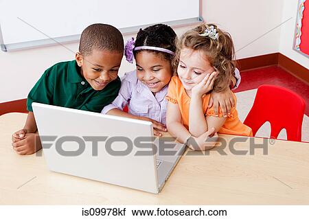 Stock Image - Three children looking at the laptop together. Fotosearch
