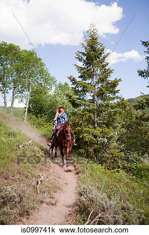 Stock Image - Woman horse riding through Beaver Creek, Colorado, USA. Fotosearch