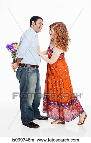 Picture - Woman looking for flowers behind man's back against white background. Fotosearch