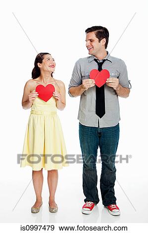 Stock Photo - Young couple holding heart shapes against white background. Fotosearch