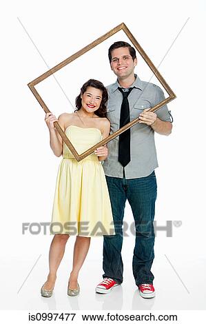 Young couple holding picture frame against white background View Large Photo Image Stock Photo - Young couple holding picture frame against white background. Fotosearch