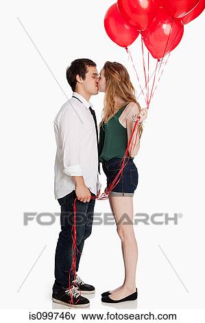 Stock Photo - Young couple kissing and holding balloons against white background. Fotosearch