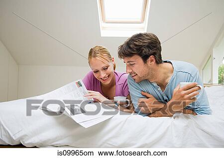 Picture - Young couple reading magazine on bed. Fotosearch