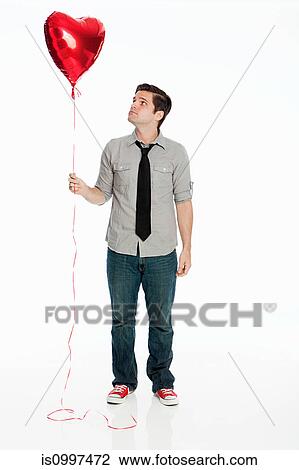 Stock Image - Young man holding balloon against white background. Fotosearch