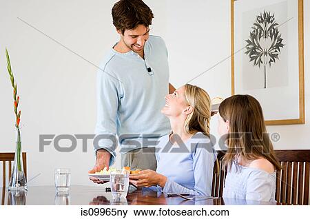 Stock Photo - Young man serving food to family. Fotosearch