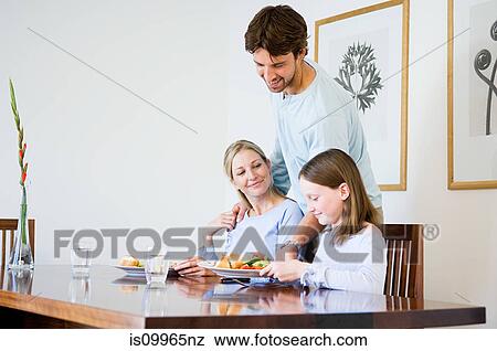 Stock Photo - Young man serving food to family. Fotosearch