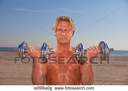Stock Image - Bare-chested man on beach with weights. Fotosearch