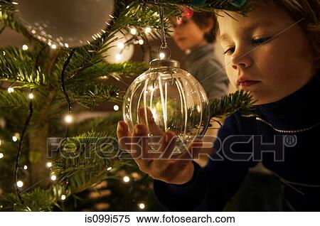 Boy decorating Christmas tree with baubles at home View Large Photo Image Stock Photography - Boy decorating Christmas tree with baubles at home. Fotosearch