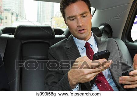 Stock Image - Businessman in car with smartphone. Fotosearch
