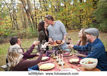 Picture - Couple kissing at outdoor dinner with friends. Fotosearch