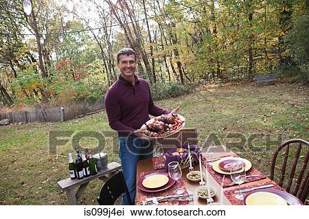 Stock Image - Mature man with food for outdoor dinner. Fotosearch