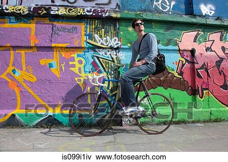 Mid adult cyclist sitting by graffiti View Large Photo Image Stock Photo - Mid adult cyclist sitting by graffiti. Fotosearch