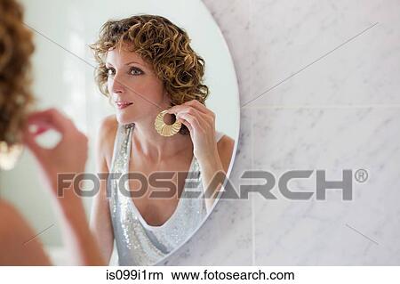 Mid adult woman putting on earrings in mirror View Large Photo Image Picture - Mid adult woman putting on earrings in mirror. Fotosearch