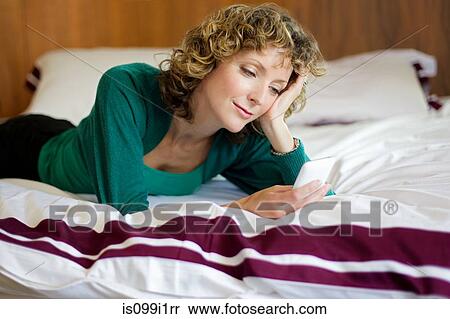 Stock Photography - Mid adult woman using cellphone in bedroom. Fotosearch
