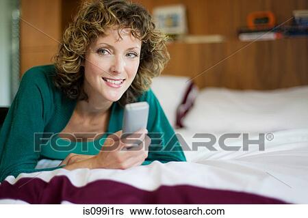 Stock Photograph - Mid adult woman using telephone in bedroom. Fotosearch