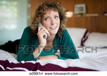 Stock Photograph - Mid adult woman using telephone in bedroom. Fotosearch