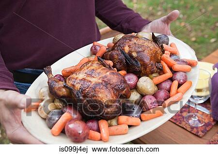Stock Image - Person holding platter of poultry and vegetables. Fotosearch