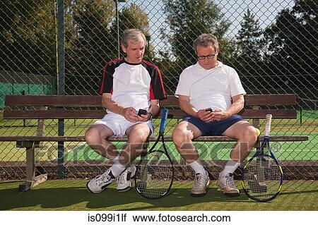 Stock Image - Senior and mature men texting on tennis court. Fotosearch