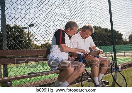 Stock Image - Senior and mature men using digital tablet on tennis court. Fotosearch