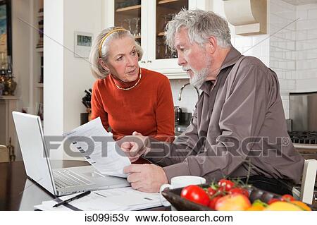 Stock Photo - Senior couple looking concerned with bills and laptop. Fotosearch