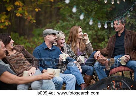Stock Photograph - Smiling friends outdoors by fire. Fotosearch