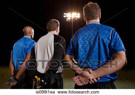Stock Image - Soccer players standing in line on pitch at night. Fotosearch
