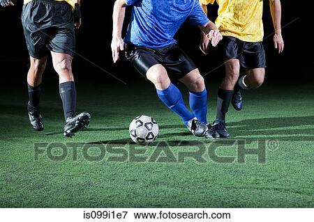 Stock Photo - Soccer players tackling on pitch, low section. Fotosearch