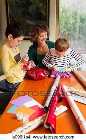 Picture - Woman and sons wrapping gifts at table. Fotosearch