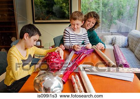 Stock Image - Woman and sons wrapping gifts at table. Fotosearch