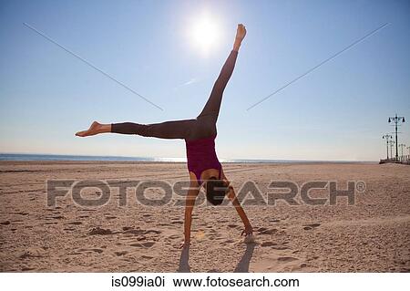 Stock Image - Woman cartwheeling on beach. Fotosearch