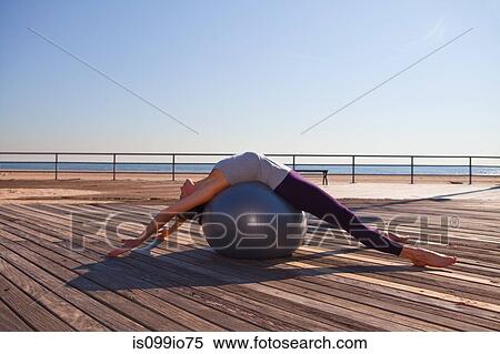 Stock Photography - Woman lying over exercise ball on promenade. Fotosearch