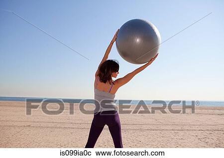Stock Image - Woman on beach using exercise ball. Fotosearch