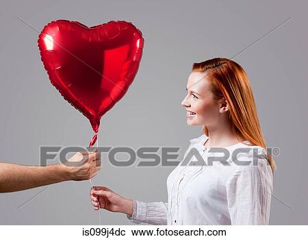 Stock Image - Young woman being given heart shaped balloon. Fotosearch