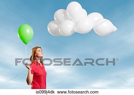 Stock Image - Young woman looking at cloud made of balloons. Fotosearch