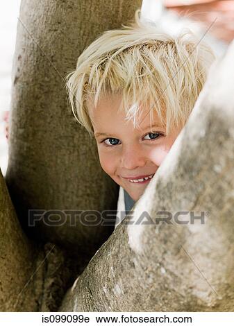 Stock Image - Boy peeking from behing tree, portrait. Fotosearch
