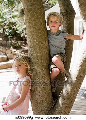 Stock Image - Brother and sister climbing tree. Fotosearch