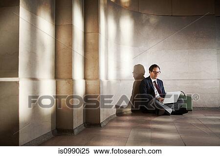Stock Photography - Businessman sitting on floor by wall using laptop. Fotosearch