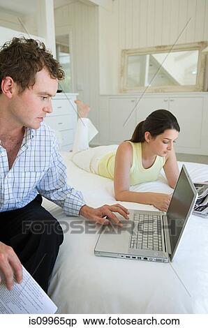 Stock Photography - Couple on bed, man using laptop. Fotosearch