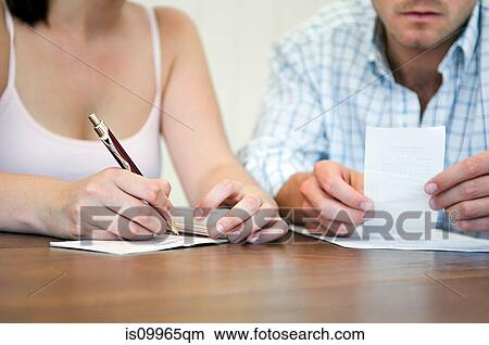 Picture - Couple planning home finances, woman writing cheque. Fotosearch
