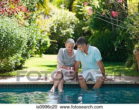 Stock Image - Couple sitting at poolside in garden. Fotosearch