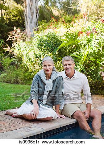 Stock Photography - Couple sitting at poolside, portrait. Fotosearch
