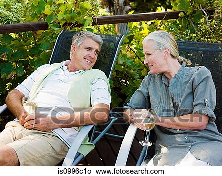 Picture - Couple sitting on garden chairs with wine. Fotosearch