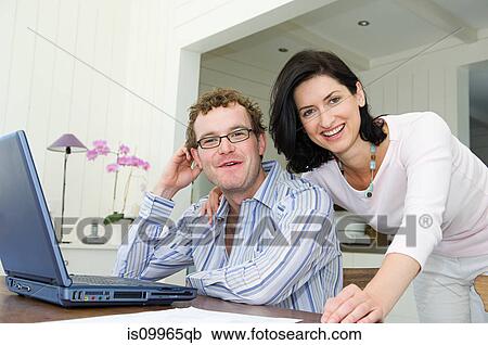 Stock Image - Couple using laptop in kitchen. Fotosearch