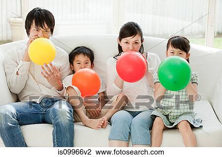 Stock Image - Family with two children blowing up balloons. Fotosearch