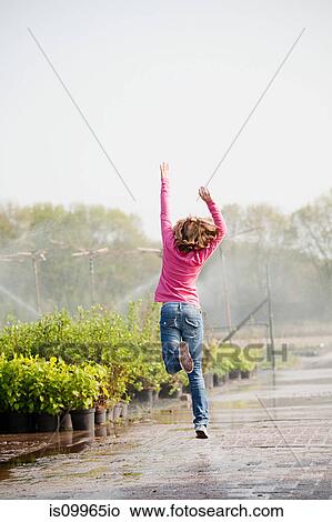 Picture - Girl skipping along path in plant nursery. Fotosearch