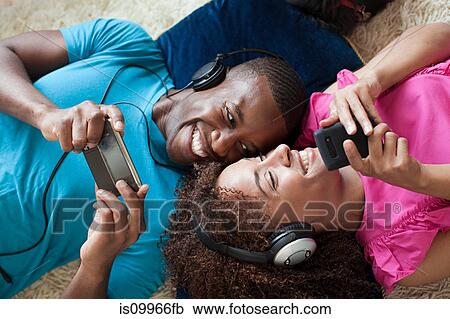 Stock Image - Man and woman playing on handheld device and smartphone. Fotosearch