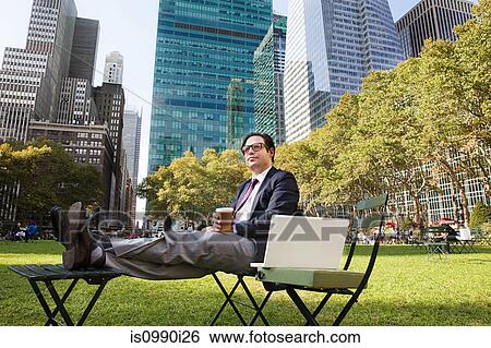 Man sitting in park with coffee and laptop View Large Photo Image Stock Photograph - Man sitting in park with coffee and laptop. Fotosearch