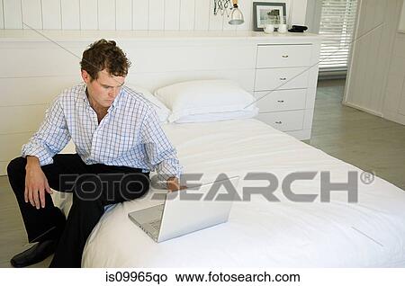 Man sitting on bed using laptop View Large Photo Image Picture - Man sitting on bed using laptop. Fotosearch