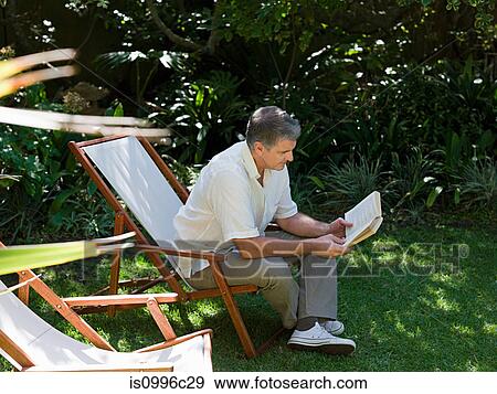 Stock Photo - Man sitting on deckchair in garden reading book. Fotosearch
