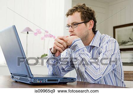 Stock Photo - Man using laptop in kitchen. Fotosearch